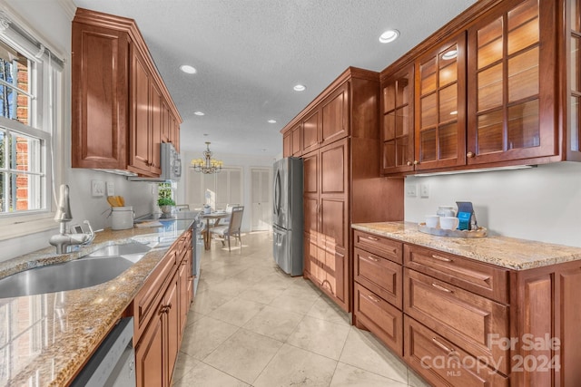 kitchen with a textured ceiling, light stone counters, sink, and stainless steel appliances