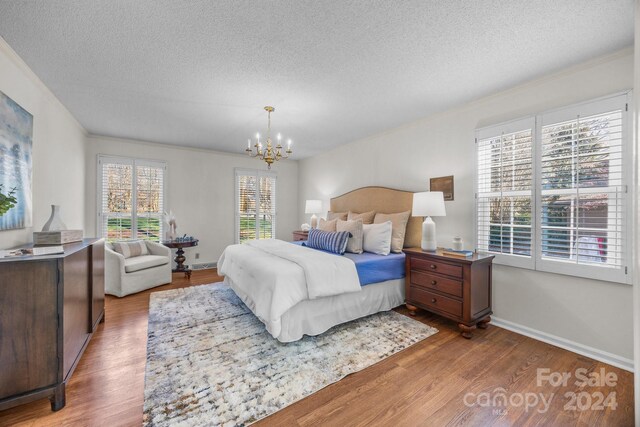 bedroom with wood-type flooring, a textured ceiling, and an inviting chandelier