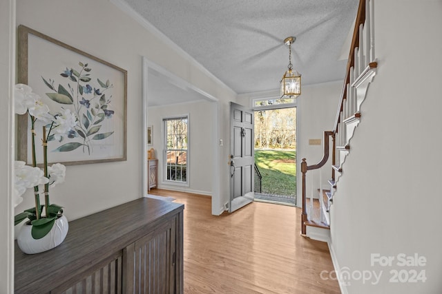 foyer featuring light wood-type flooring, a textured ceiling, and ornamental molding