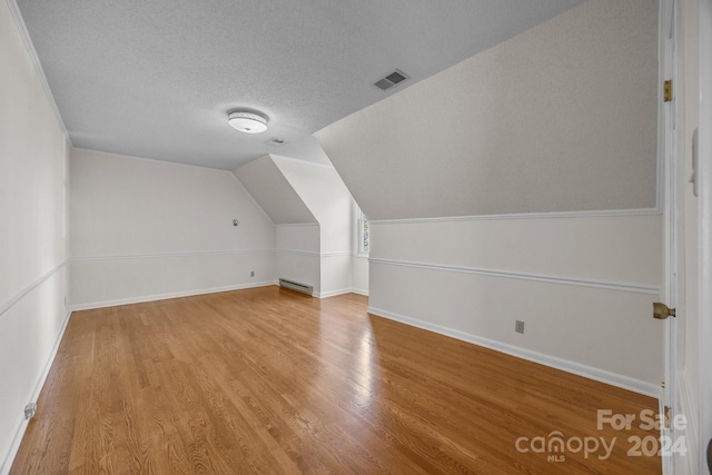 additional living space featuring hardwood / wood-style floors, a textured ceiling, a baseboard radiator, and vaulted ceiling