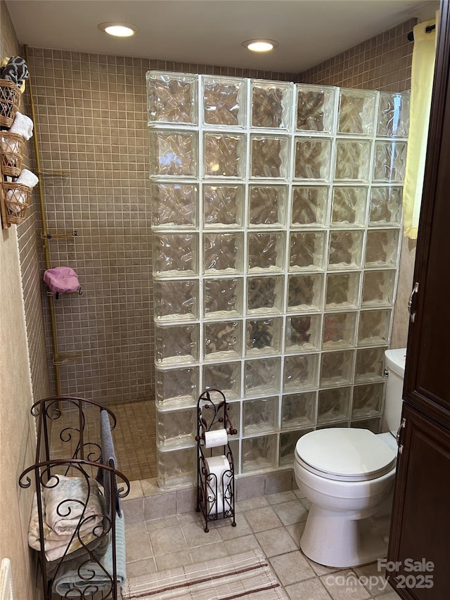 bathroom with a tile shower, tile patterned floors, tile walls, and toilet