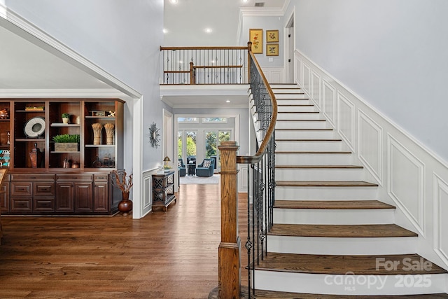 stairs featuring wood-type flooring, crown molding, and a high ceiling