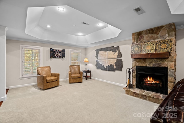 living area featuring a stone fireplace, ornamental molding, carpet floors, and a tray ceiling