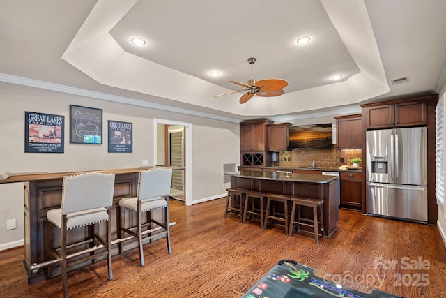 kitchen featuring a kitchen breakfast bar, stainless steel fridge with ice dispenser, dark hardwood / wood-style floors, a tray ceiling, and a kitchen island