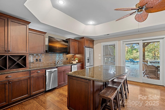 kitchen with dark stone counters, light hardwood / wood-style floors, a tray ceiling, a kitchen island, and stainless steel appliances