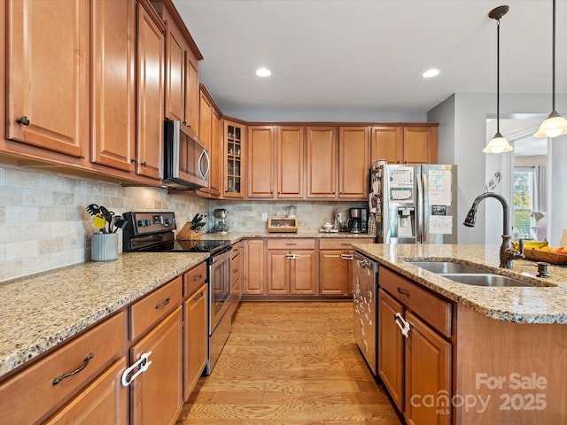 kitchen featuring sink, hanging light fixtures, light hardwood / wood-style flooring, decorative backsplash, and appliances with stainless steel finishes