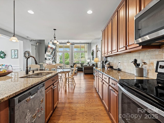 kitchen with light stone counters, sink, pendant lighting, and appliances with stainless steel finishes