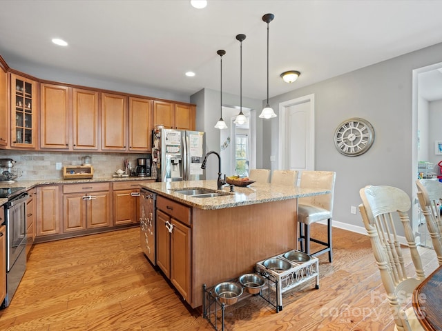 kitchen with a kitchen bar, a kitchen island with sink, sink, appliances with stainless steel finishes, and light stone counters