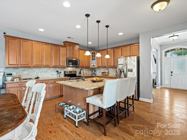 kitchen featuring light stone countertops, a kitchen bar, stainless steel appliances, sink, and an island with sink