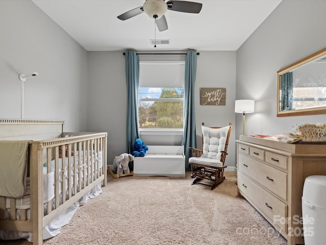 bedroom featuring light colored carpet, a nursery area, and ceiling fan