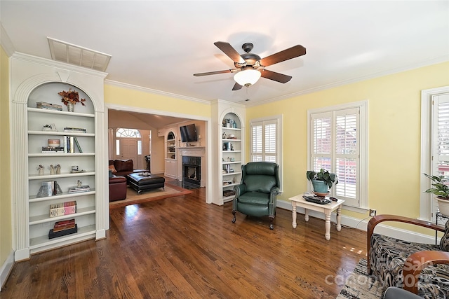 living area featuring ceiling fan, built in shelves, dark hardwood / wood-style floors, and ornamental molding