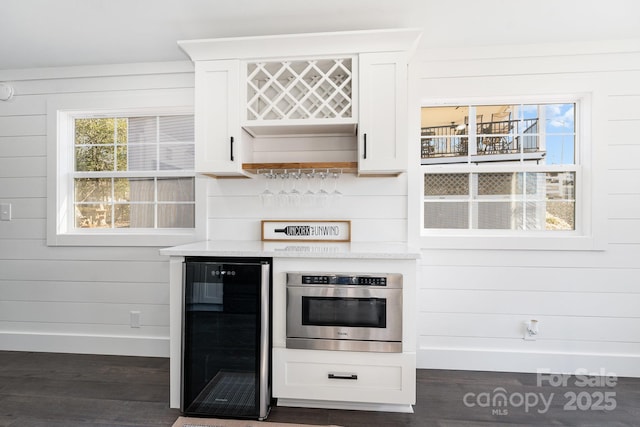 kitchen featuring wine cooler, white cabinetry, dark hardwood / wood-style floors, oven, and wood walls