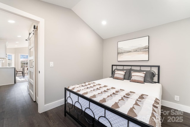 bedroom with dark hardwood / wood-style flooring, a barn door, and vaulted ceiling