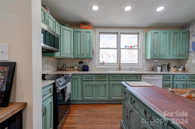 kitchen with electric range, sink, dishwasher, green cabinets, and light wood-type flooring