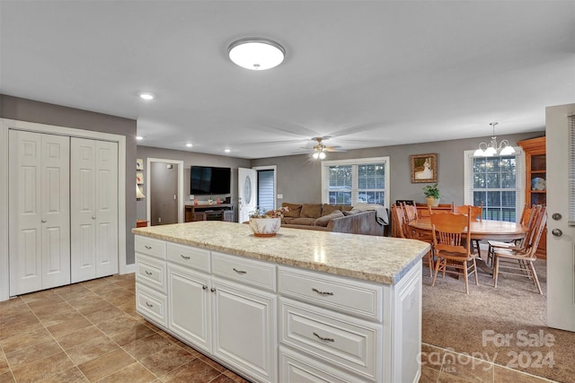 kitchen with ceiling fan with notable chandelier, light colored carpet, decorative light fixtures, a center island, and white cabinetry