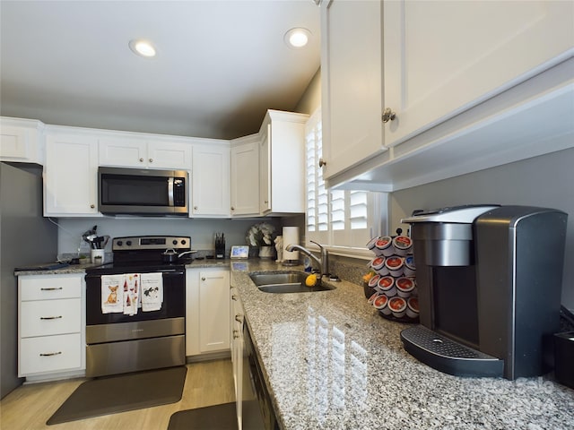 kitchen with white cabinets, stainless steel appliances, light stone counters, and sink