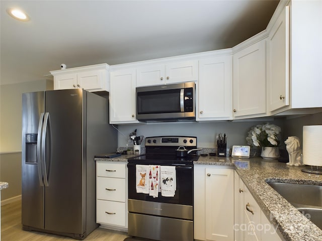 kitchen featuring dark stone counters, sink, appliances with stainless steel finishes, light hardwood / wood-style floors, and white cabinetry