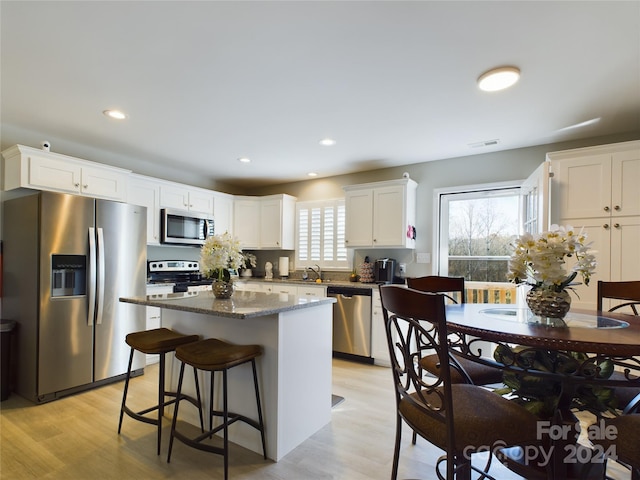 kitchen featuring stainless steel appliances, sink, light hardwood / wood-style flooring, white cabinets, and a kitchen island