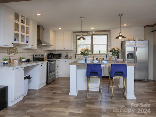 kitchen featuring a center island, hanging light fixtures, wall chimney exhaust hood, white cabinetry, and stainless steel appliances