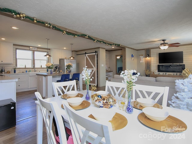 dining room featuring a textured ceiling, ceiling fan, dark wood-type flooring, sink, and a barn door