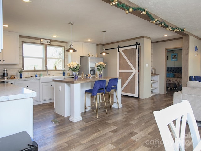 kitchen with stainless steel refrigerator with ice dispenser, pendant lighting, a barn door, white cabinets, and a kitchen island