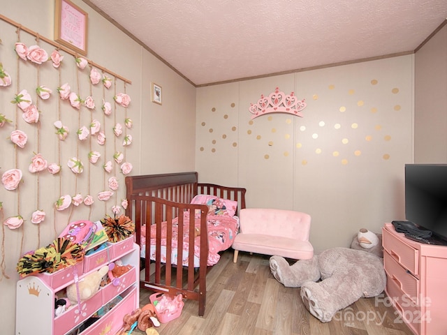 bedroom with a crib, a textured ceiling, light hardwood / wood-style floors, and crown molding