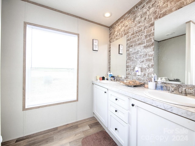 bathroom featuring hardwood / wood-style floors, vanity, a healthy amount of sunlight, and brick wall