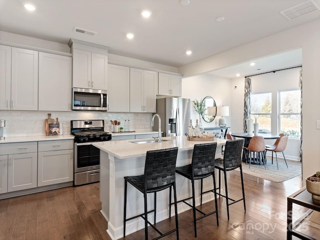 kitchen with a kitchen breakfast bar, stainless steel appliances, a kitchen island with sink, dark wood-type flooring, and sink