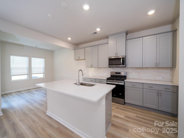 kitchen featuring gray cabinetry, sink, an island with sink, and stainless steel appliances