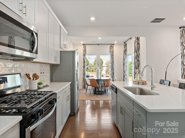 kitchen featuring sink, dark hardwood / wood-style floors, backsplash, a kitchen island with sink, and appliances with stainless steel finishes