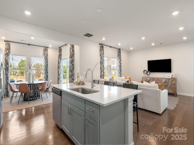 kitchen with gray cabinetry, sink, stainless steel dishwasher, an island with sink, and dark hardwood / wood-style flooring