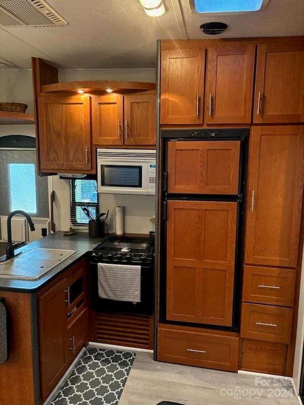 kitchen with sink, white microwave, light hardwood / wood-style floors, and black range