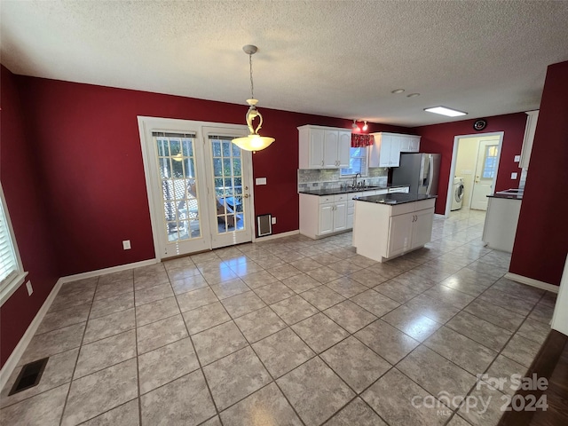 kitchen with hanging light fixtures, stainless steel refrigerator with ice dispenser, independent washer and dryer, backsplash, and white cabinets