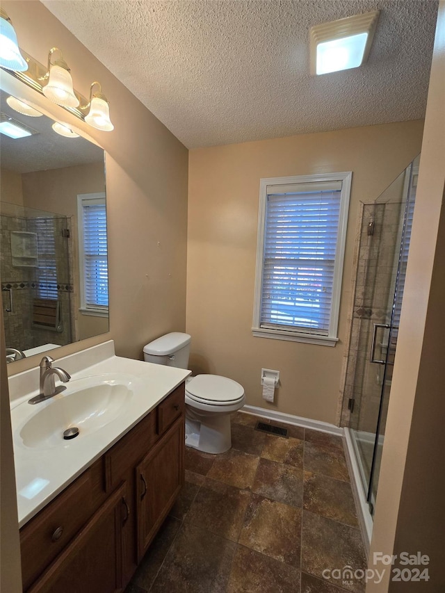 bathroom featuring a textured ceiling, vanity, toilet, and walk in shower