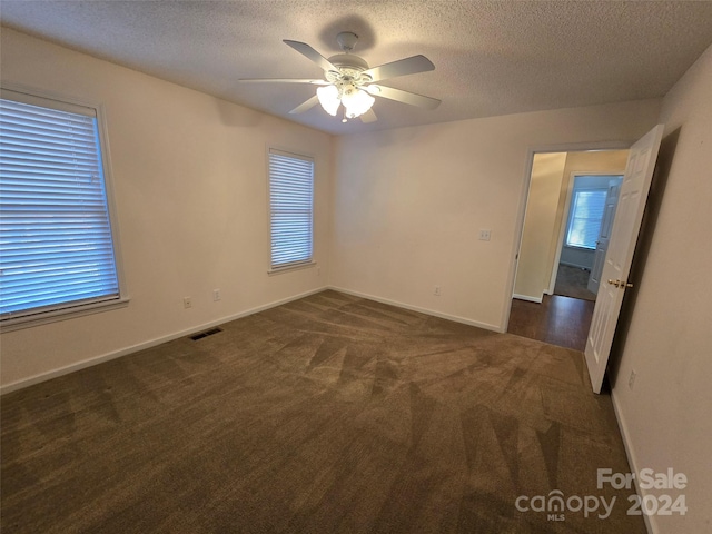 empty room featuring dark colored carpet, ceiling fan, and a textured ceiling