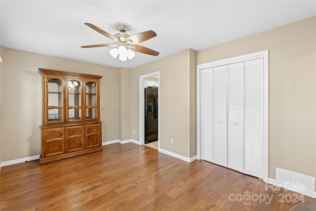 unfurnished bedroom featuring ceiling fan, wood-type flooring, black refrigerator with ice dispenser, and a closet