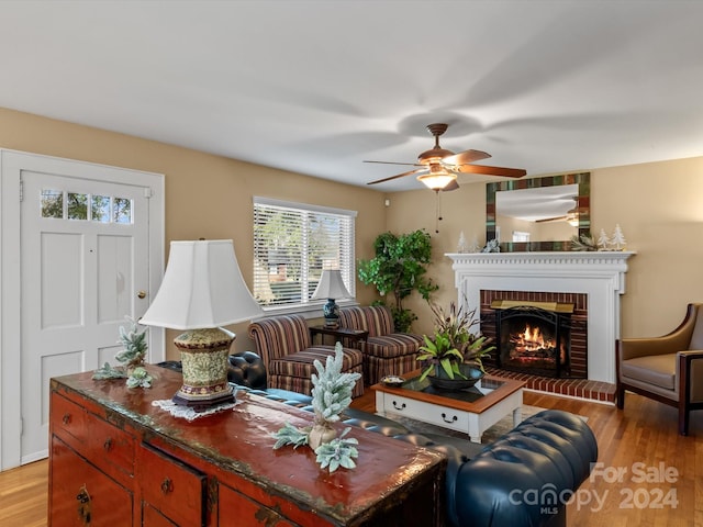 living room with ceiling fan, light wood-type flooring, and a brick fireplace