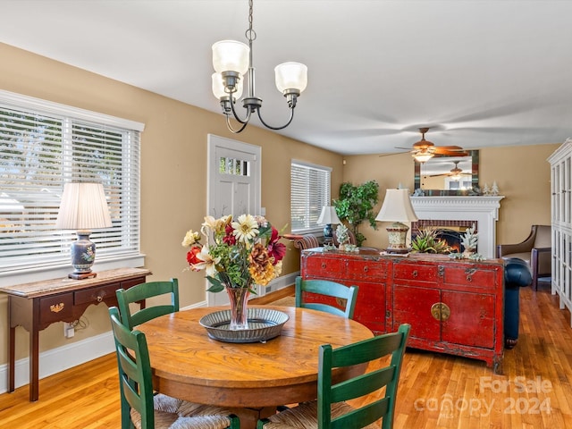 dining space with a fireplace, light hardwood / wood-style floors, and ceiling fan with notable chandelier