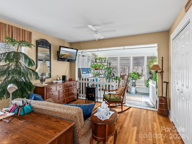 living area with a wood stove, light hardwood / wood-style flooring, and ceiling fan