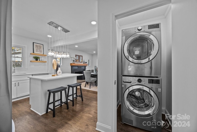 laundry area featuring sink, ornamental molding, stacked washer / dryer, and dark wood-type flooring