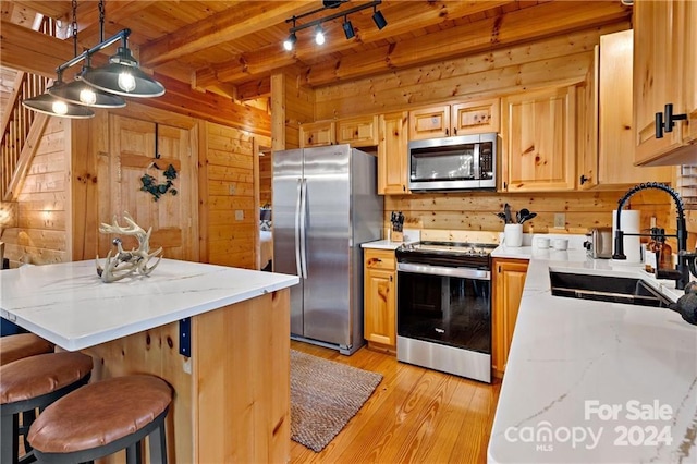 kitchen featuring stainless steel appliances, wooden walls, sink, pendant lighting, and beamed ceiling