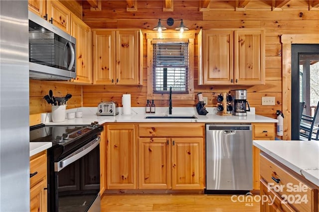 kitchen with wood walls, sink, light wood-type flooring, and appliances with stainless steel finishes