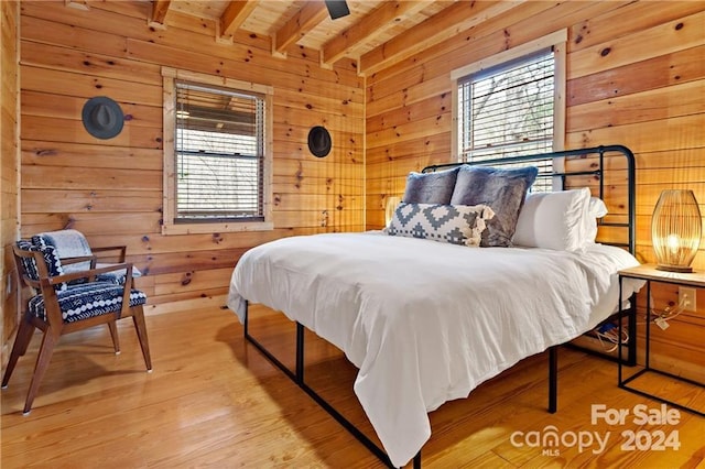 bedroom with beam ceiling, multiple windows, and wood walls