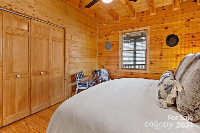 bedroom featuring beamed ceiling, ceiling fan, wood walls, and light wood-type flooring