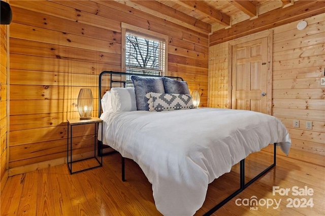 bedroom featuring beam ceiling, light wood-type flooring, wooden ceiling, and wooden walls