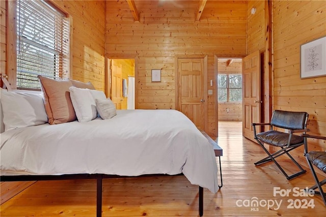 bedroom featuring beam ceiling, light hardwood / wood-style floors, wooden walls, and multiple windows