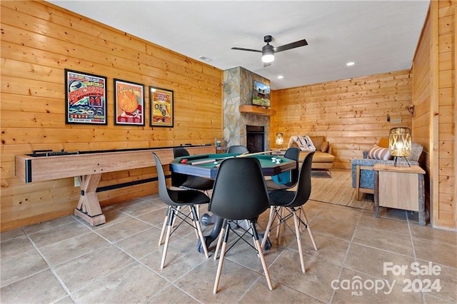 recreation room with tile patterned flooring, ceiling fan, wood walls, and a fireplace