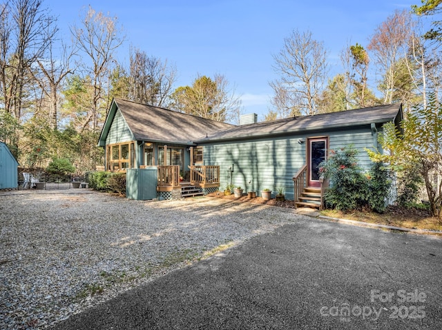 view of front facade featuring entry steps, driveway, a chimney, and a wooden deck