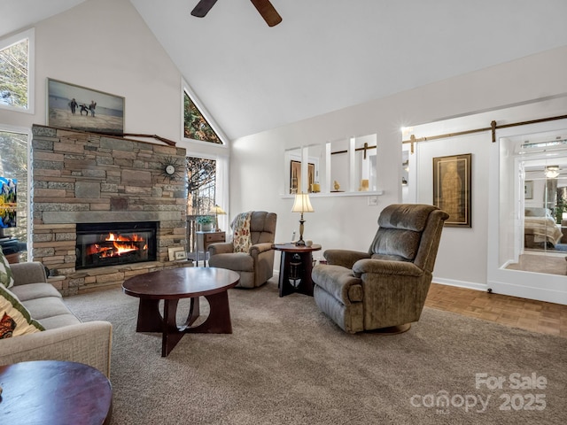 living area with a barn door, high vaulted ceiling, a ceiling fan, and a stone fireplace