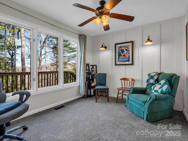 living area featuring a decorative wall, a ceiling fan, baseboards, visible vents, and carpet